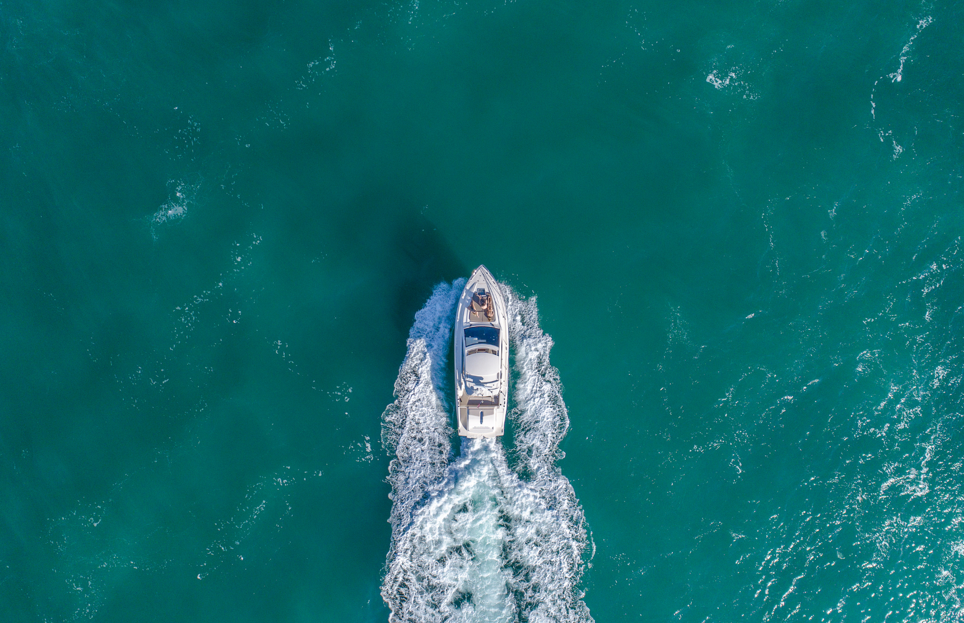 White motorboat traveling across turquoise ocean, leaving a white wake.