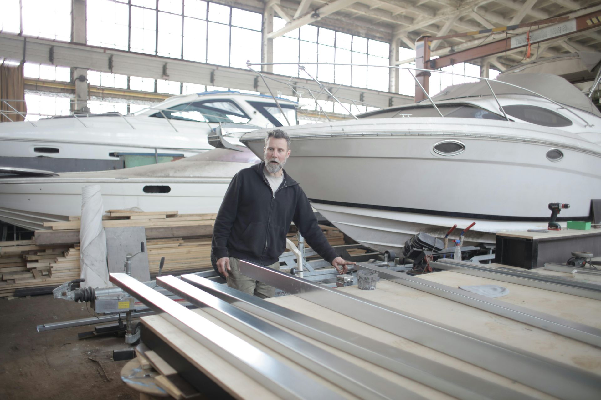 Man in workshop with boats, using saw.