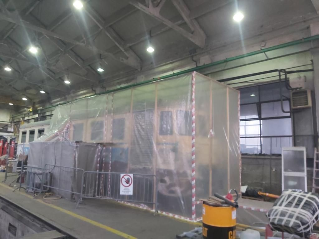 Un edificio è ricoperto di plastica e in primo piano c'è una botte gialla.