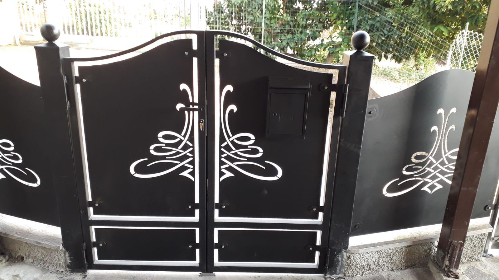 Cancello in metallo nero con volute decorative bianche e cassetta della posta.