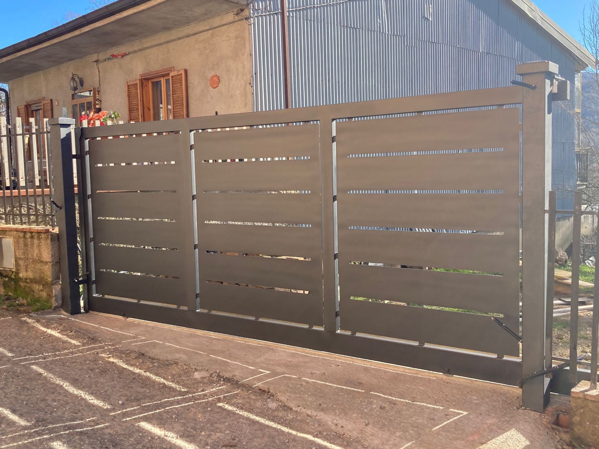 Cancello in metallo marrone con stecche orizzontali, posizionato di fronte a una casa.