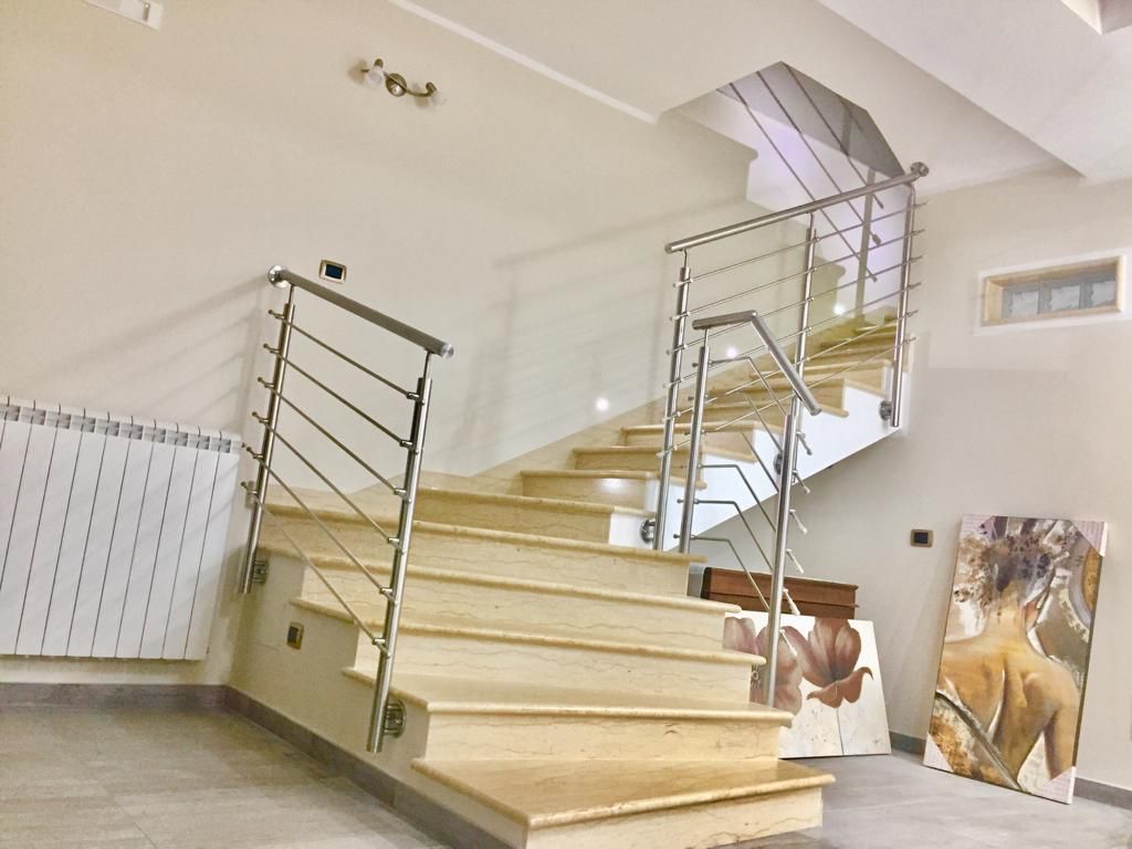 Scala con ringhiere in acciaio inox e gradini in pietra chiara. Un'opera d'arte è appoggiata a una parete.