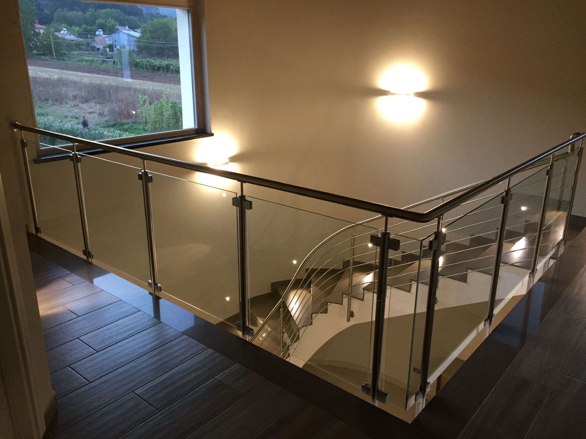 Scala moderna con ringhiera in vetro e corrimano in legno scuro, che conduce in basso.