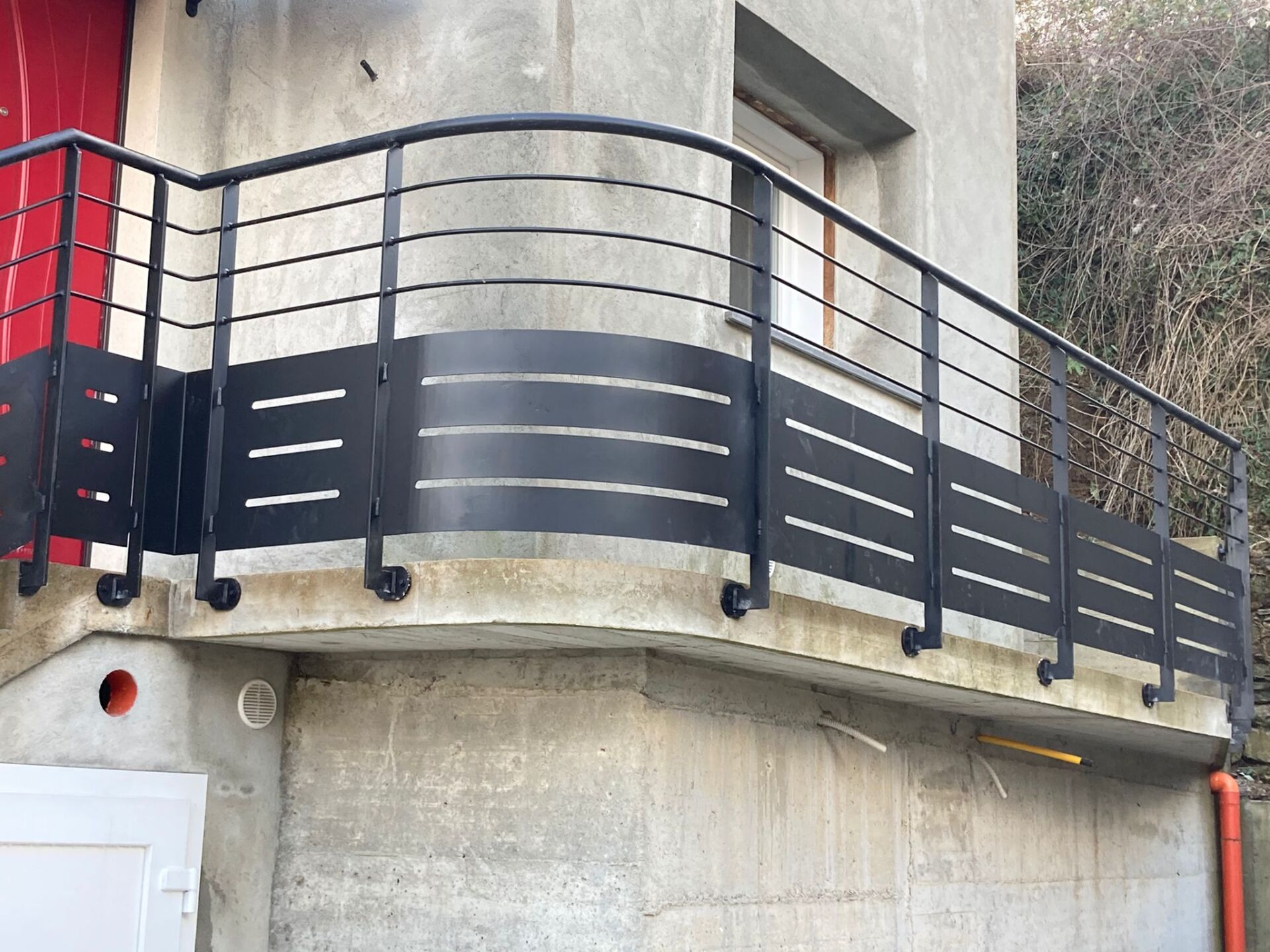 Ringhiera del balcone in metallo nero su una struttura in cemento con traversa superiore curva e barre orizzontali.
