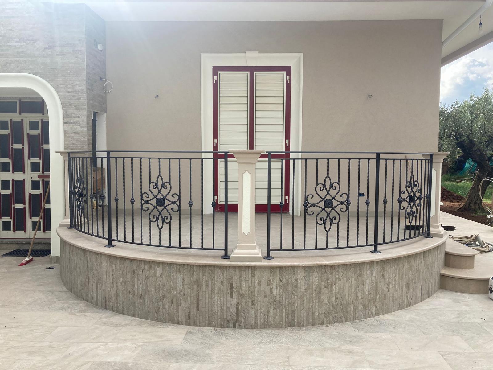 Patio curvo in pietra con ringhiera decorativa in metallo nero e una colonna beige, che conduce a una porta.
