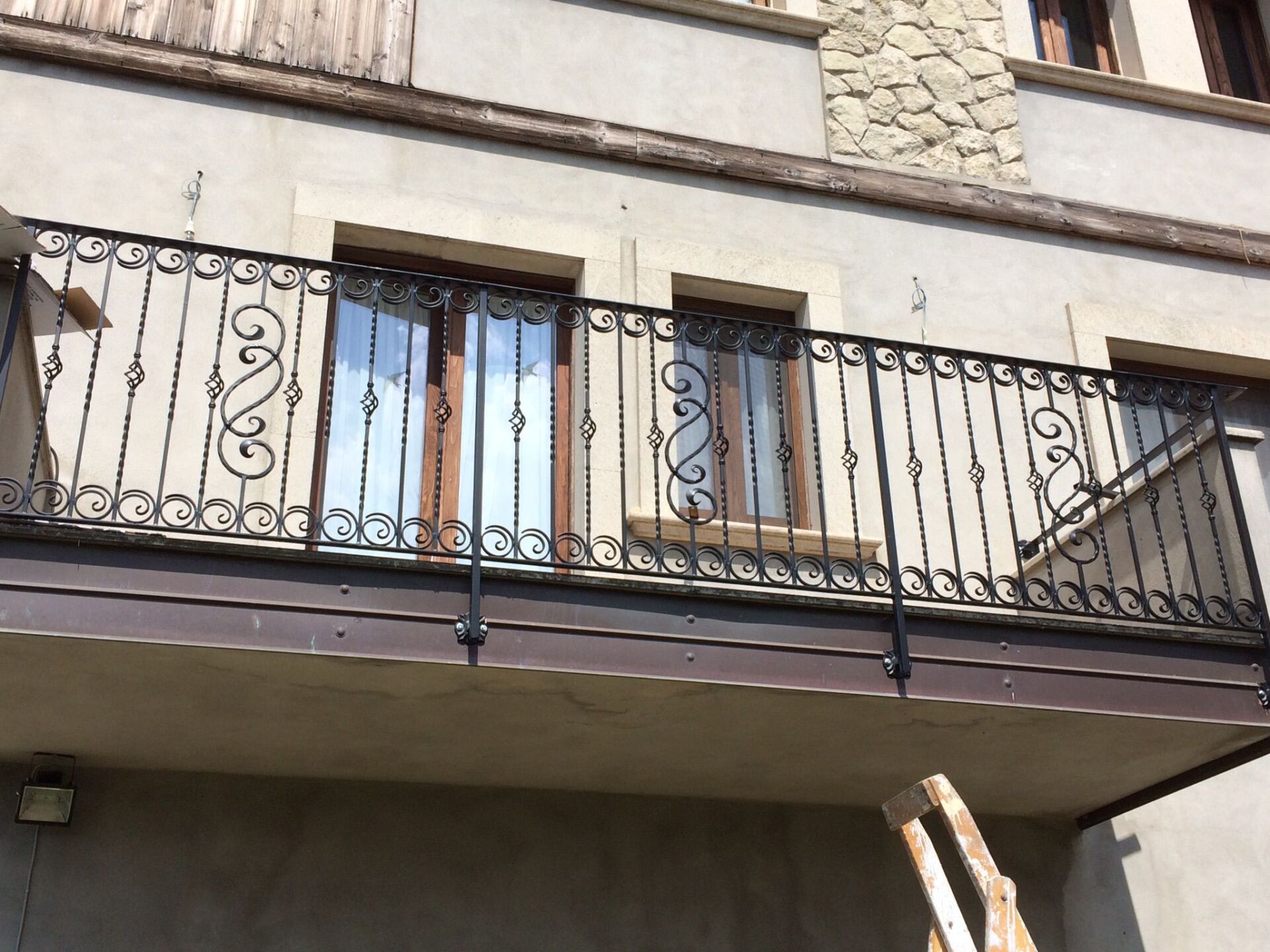 Ringhiera in ferro battuto nero del balcone davanti a due finestre di un edificio chiaro.