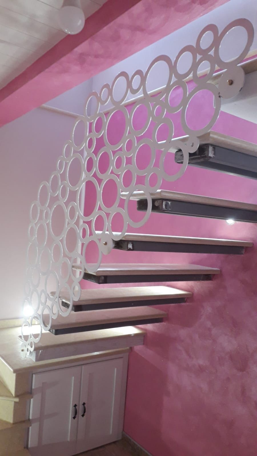 Scala a chiocciola con ringhiera circolare bianca, pareti rosa e gradini in legno.
