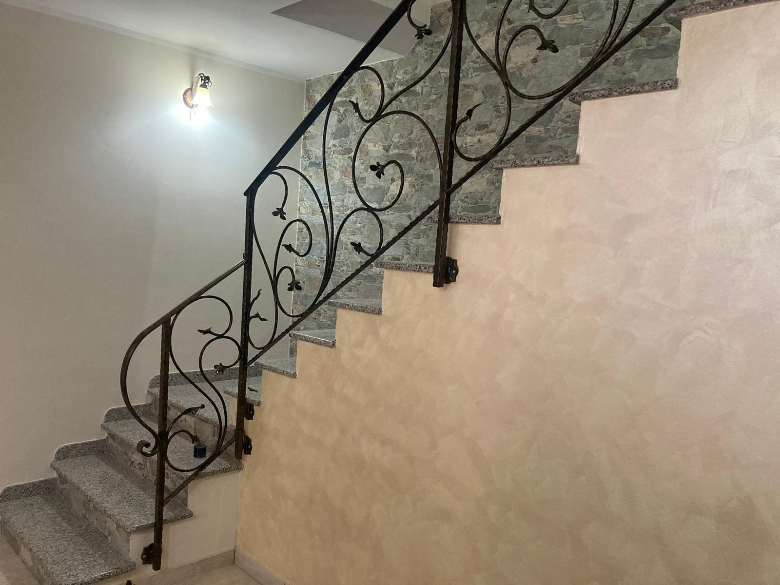 Scala con ringhiera decorativa in ferro battuto. Gradini in granito; parete testurizzata, dipinta di beige chiaro.