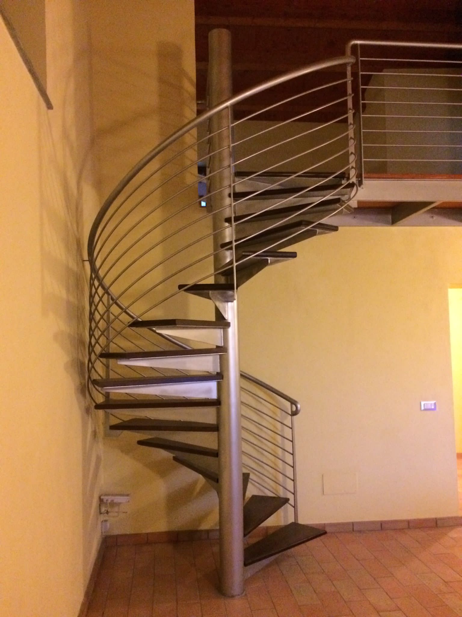 Scala a chiocciola con gradini scuri e ringhiera in acciaio inox.