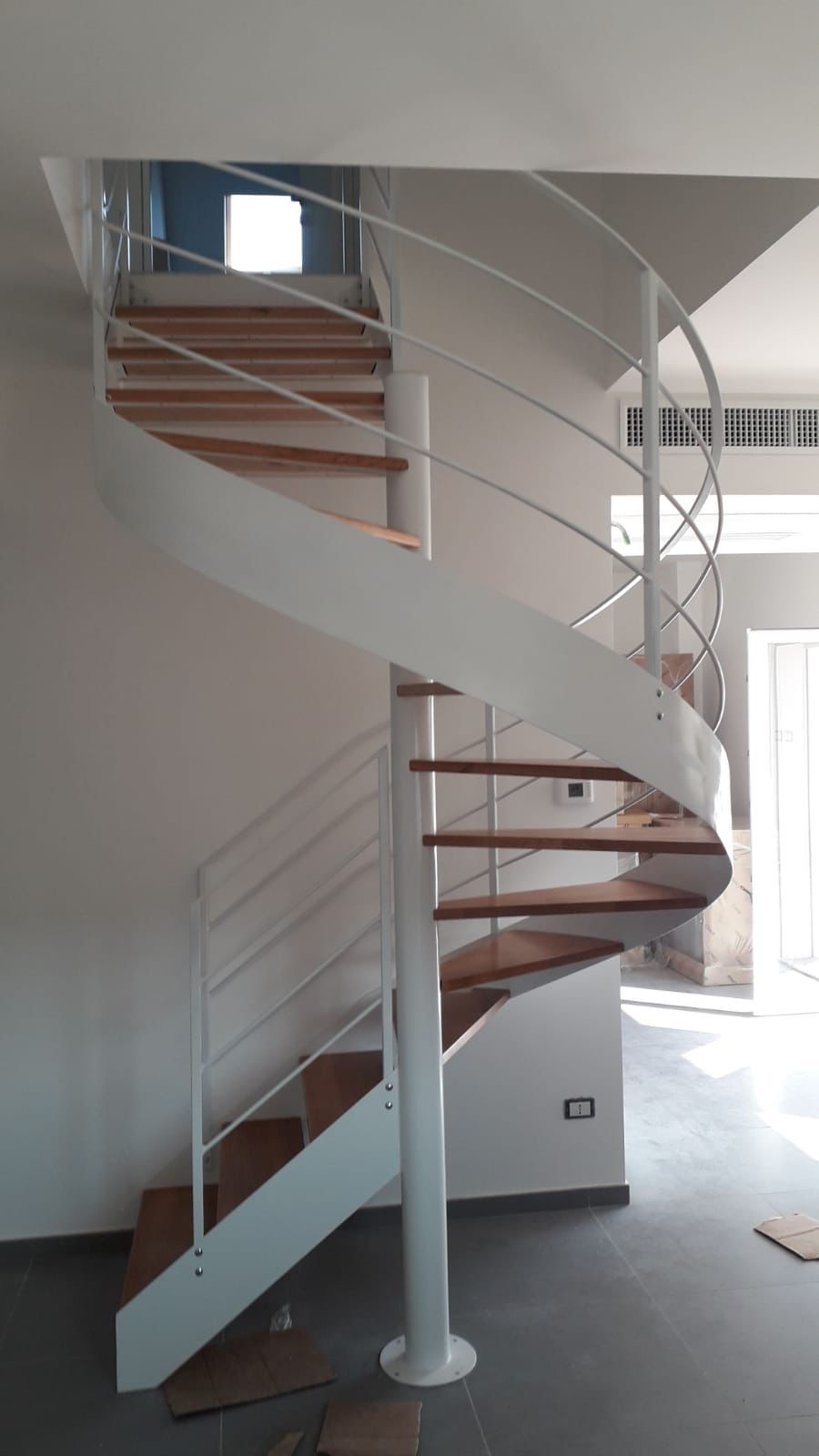 Scala a chiocciola bianca con gradini in legno, in una stanza luminosa.