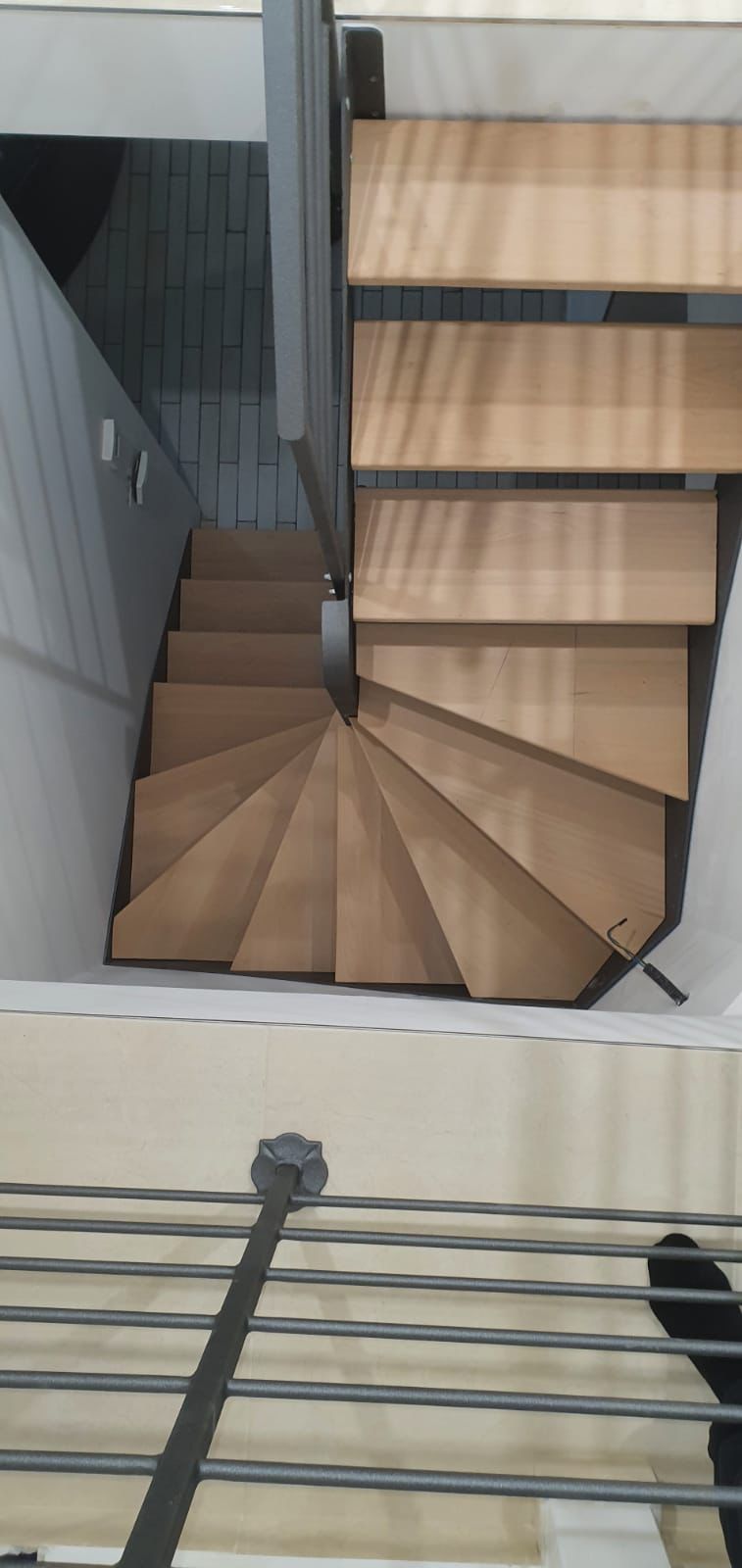 Scala a chiocciola in legno con ringhiera grigia.