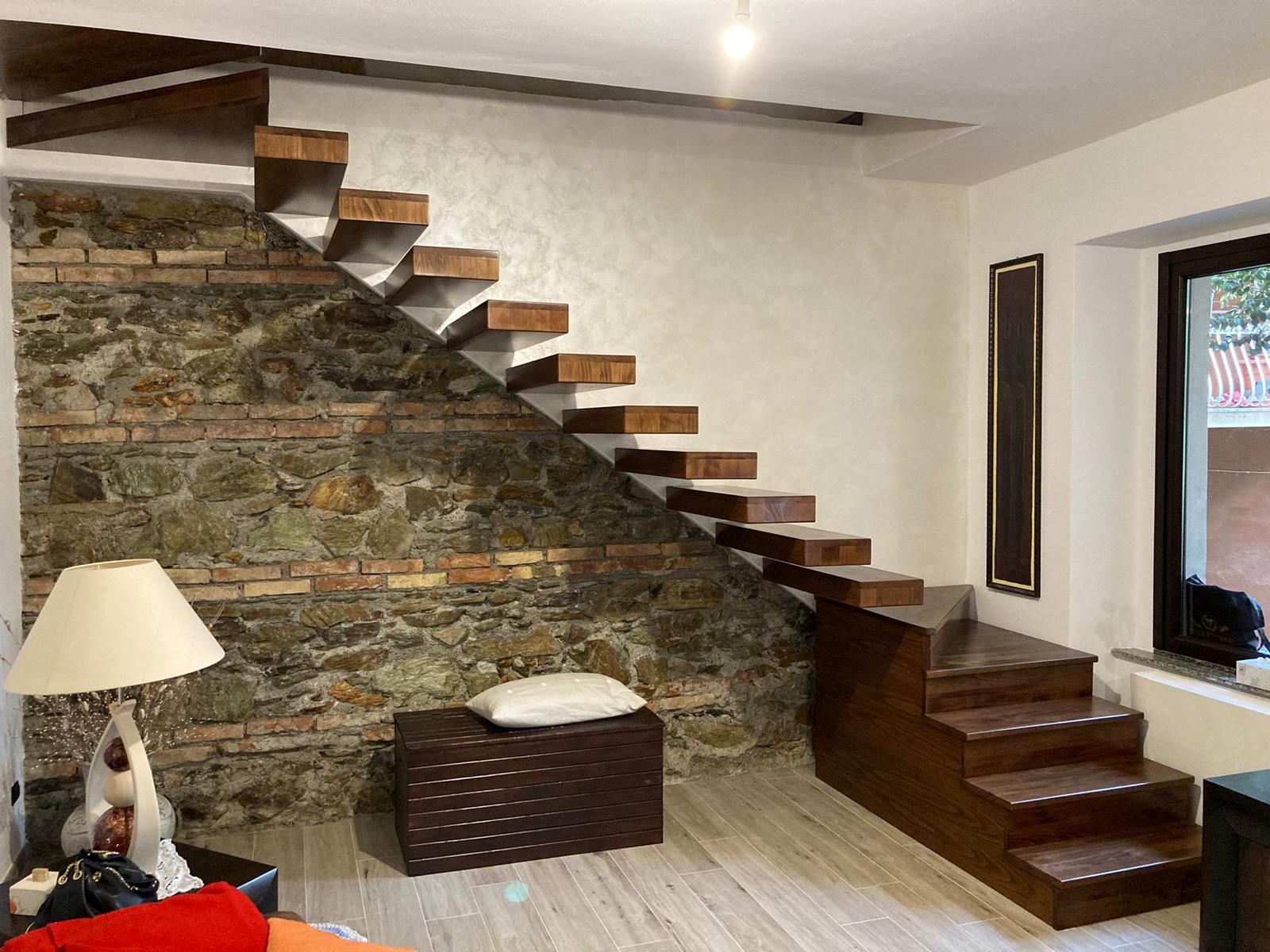 Scala in legno sospesa accanto a un muro in pietra e una piccola serie di gradini in legno.