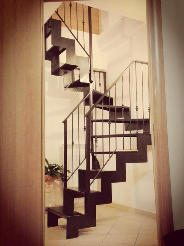 Scala a chiocciola in metallo scuro con ringhiera e gradini in legno, in un corridoio.