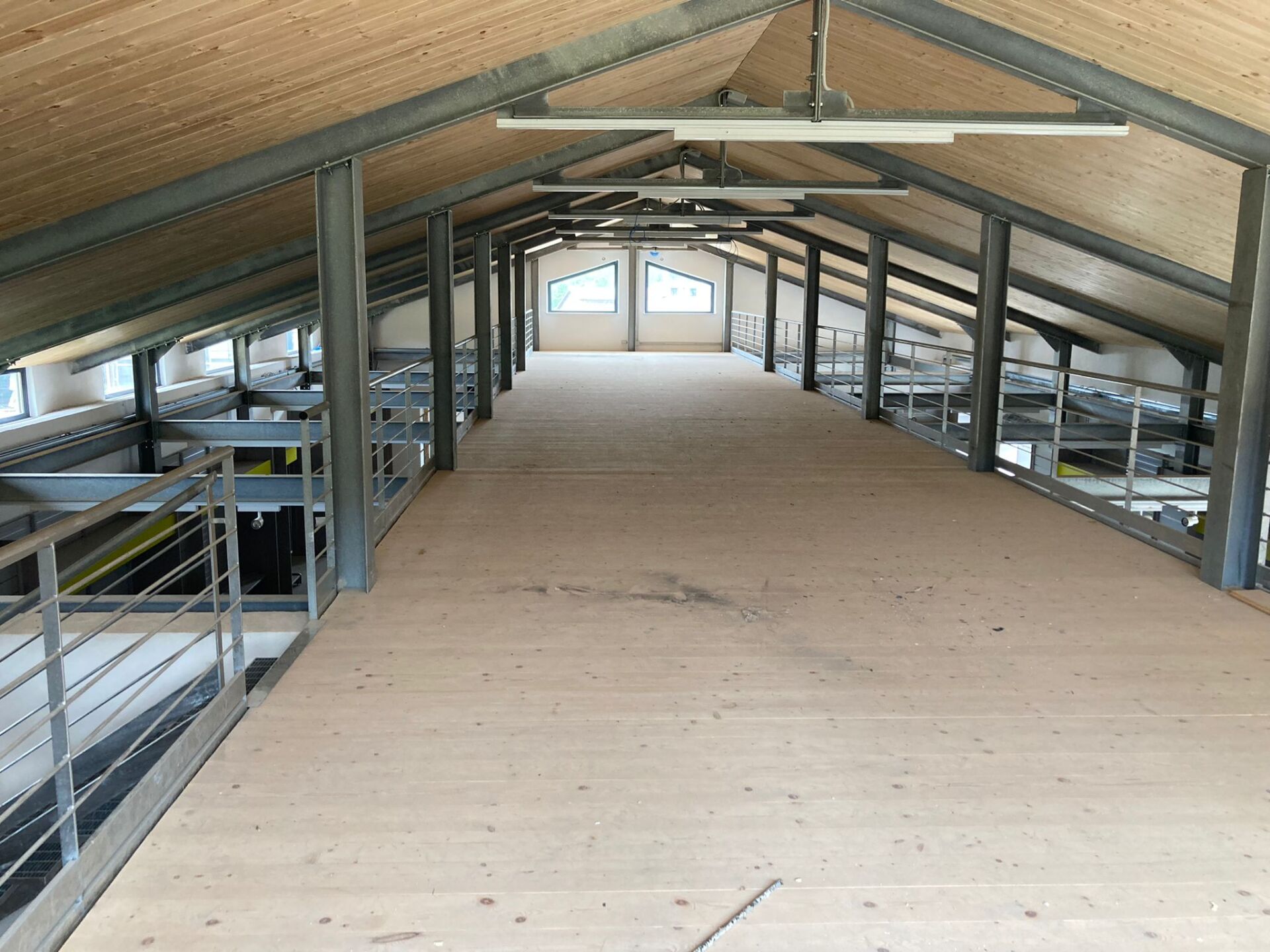 Interno del loft con travi in ​​metallo, pavimento in legno e finestre in fondo.