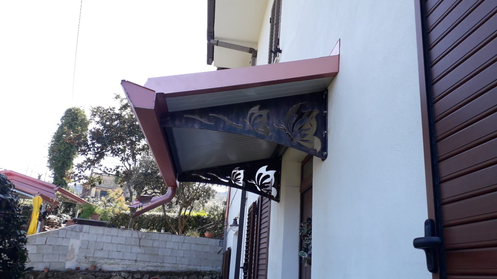 Tenda da sole in metallo marrone con motivo decorativo a foglie sopra una finestra.