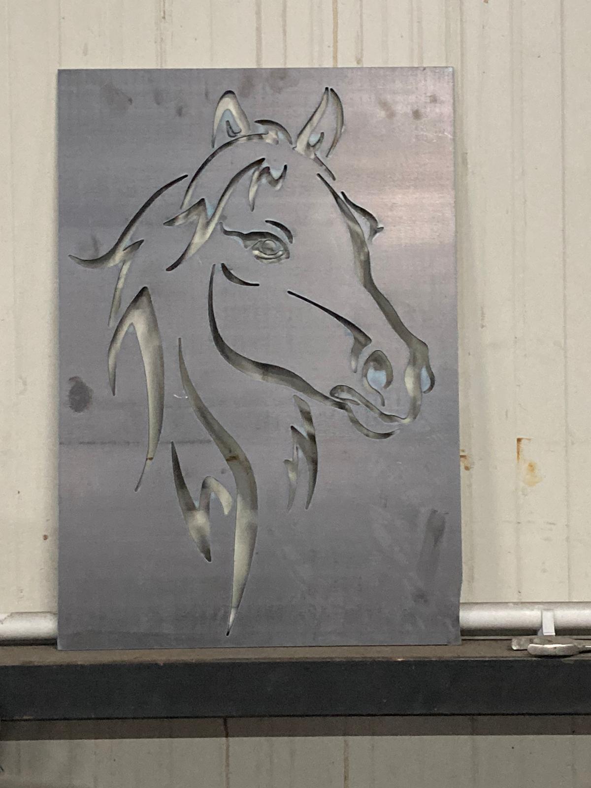 Ritaglio metallico del profilo di una testa di cavallo, montato su un foglio grigio.