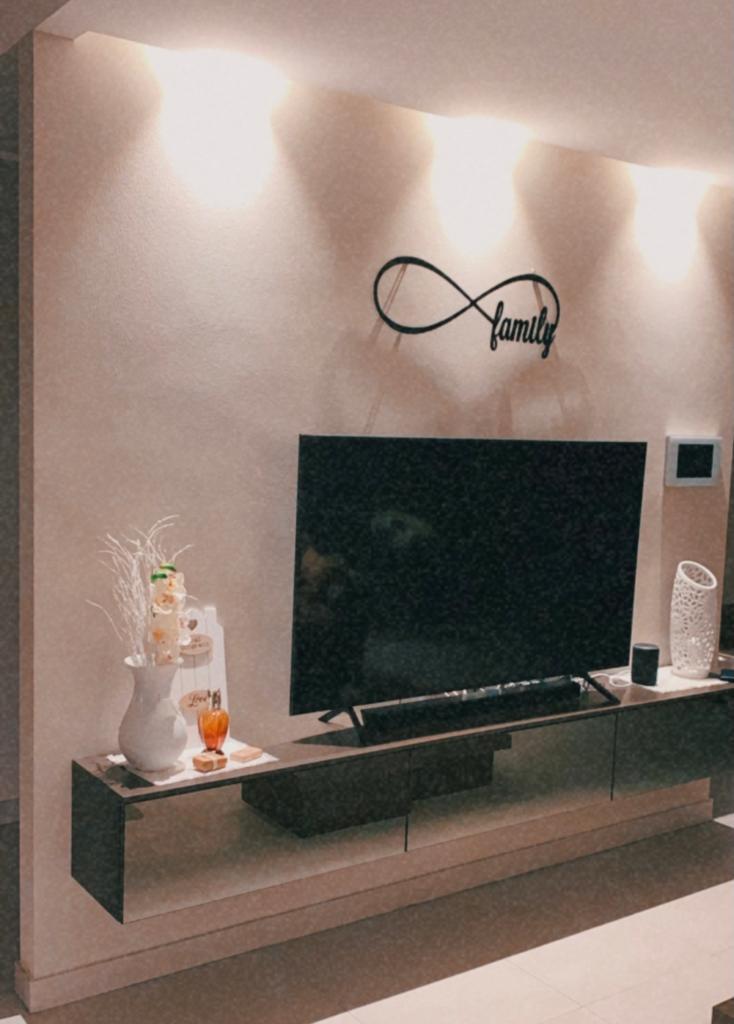 Soggiorno con TV a parete, quadro raffigurante il simbolo dell'infinito nero e mensola sospesa con decorazioni. Luci soffuse illuminano lo spazio.