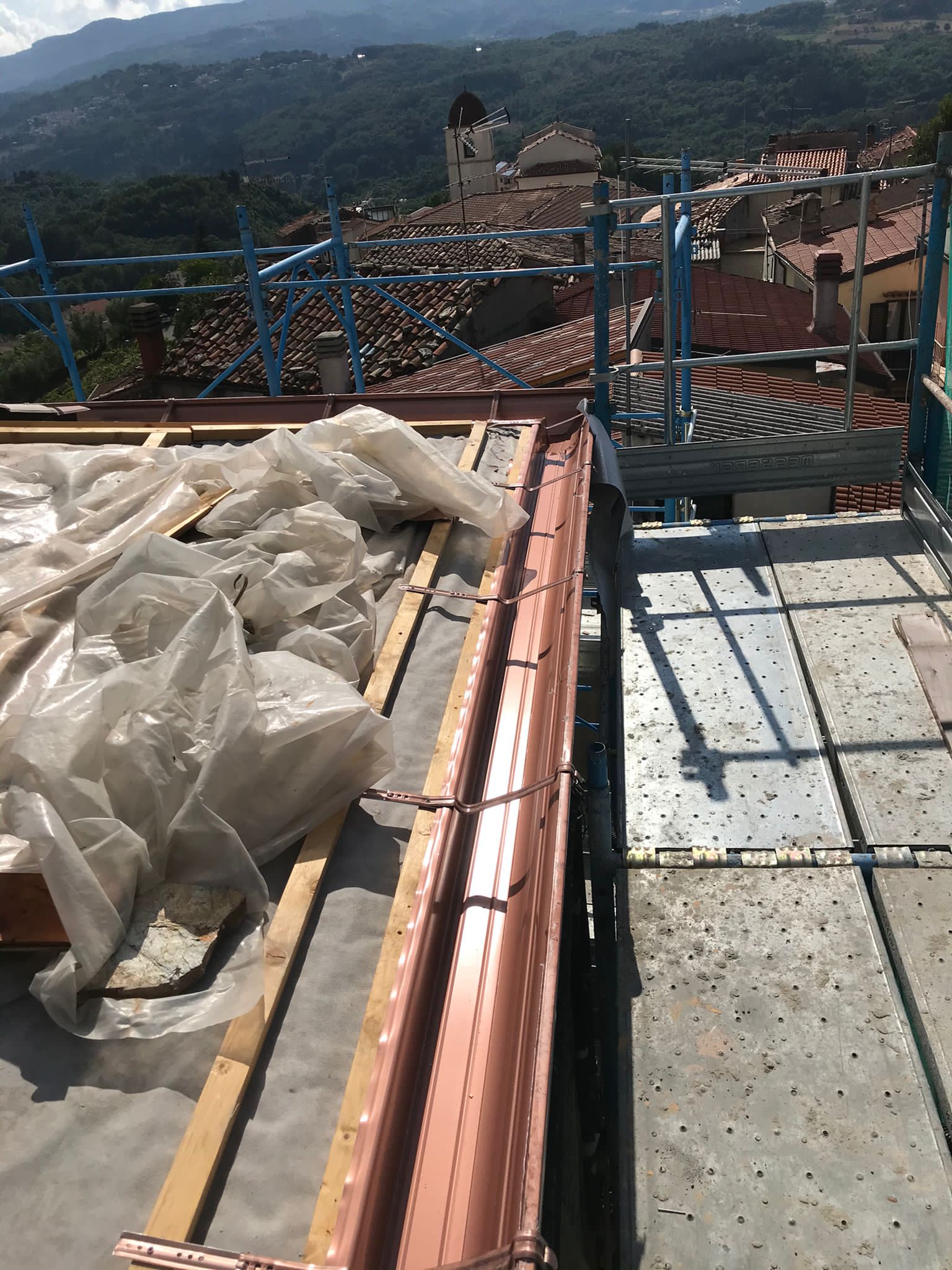 Cantiere di costruzione del tetto con grondaie in rame, impalcature e vista sui tetti di tegole e sulle montagne.
