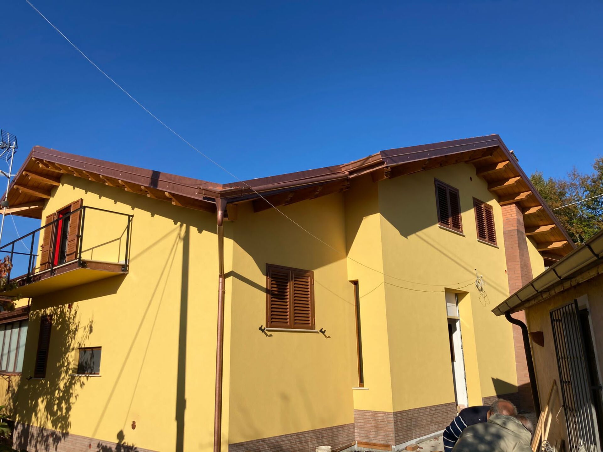 Casa gialla con tetto marrone e persiane contro un cielo blu.
