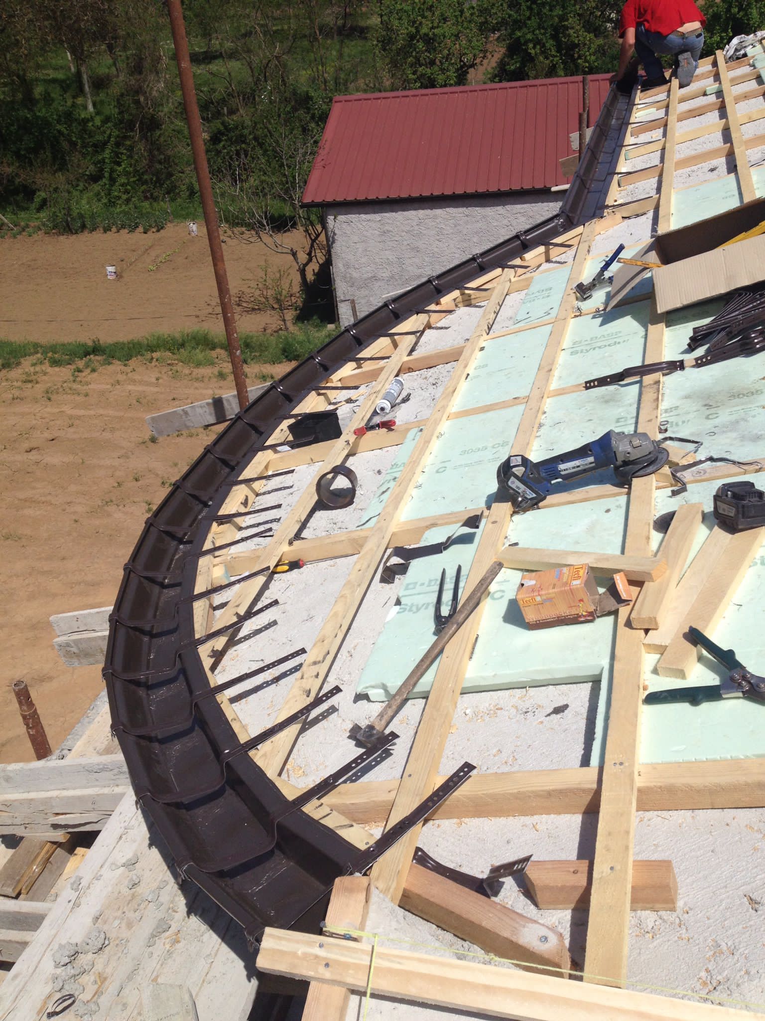 Costruzione del bordo curvo di un tetto: grondaia marrone installata, struttura in legno, isolamento, operaio.