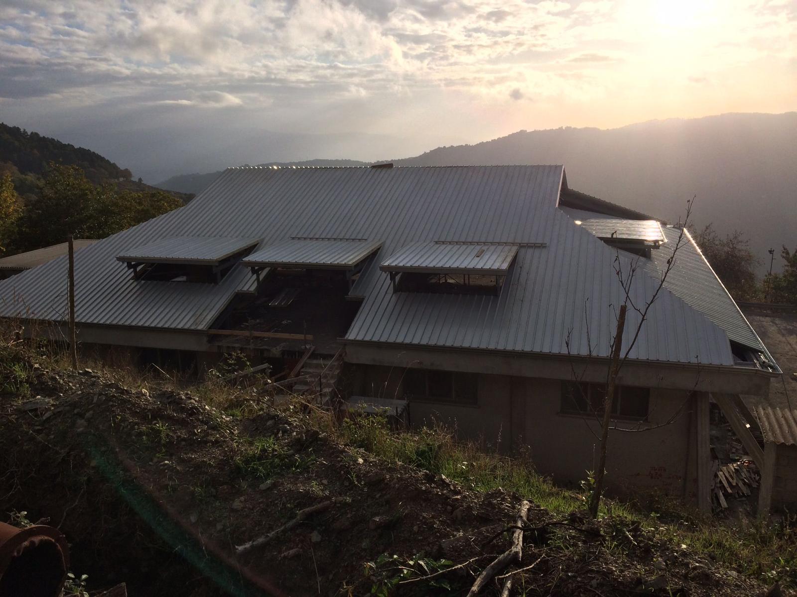 Edificio con tetto in metallo su una collina, con vista sulle montagne al tramonto.