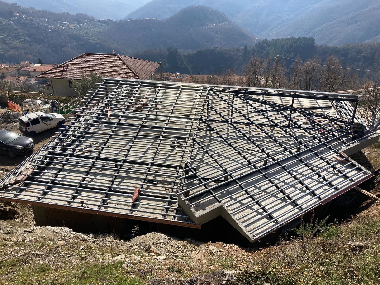 Tetto di casa parzialmente costruito con travi a vista e cemento, posizione collinare. Auto parcheggiate nelle vicinanze.
