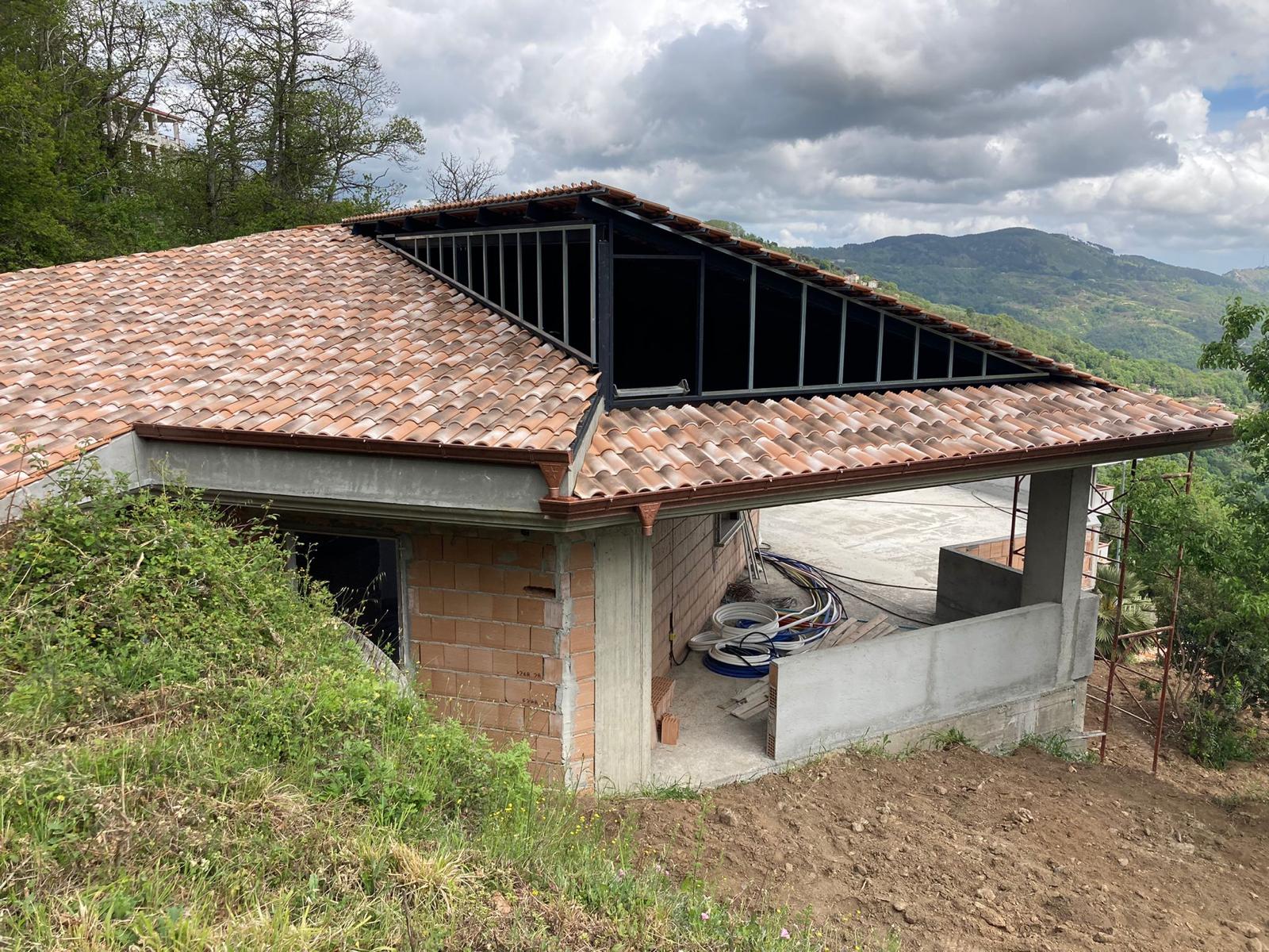 Casa parzialmente costruita con tetto in tegole rosse, muri in mattoni e montagne sullo sfondo.