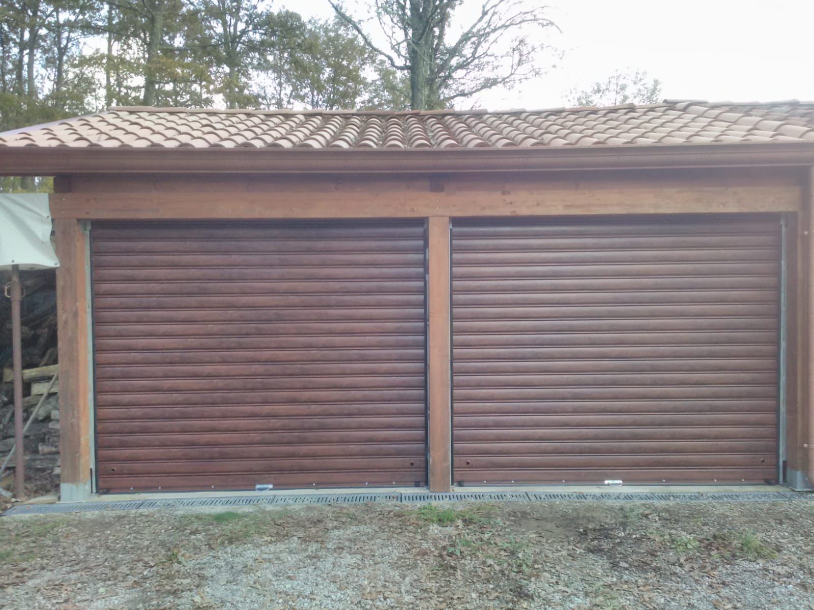 Porte da garage avvolgibili marroni sotto un tetto con struttura in legno e tegole di argilla.