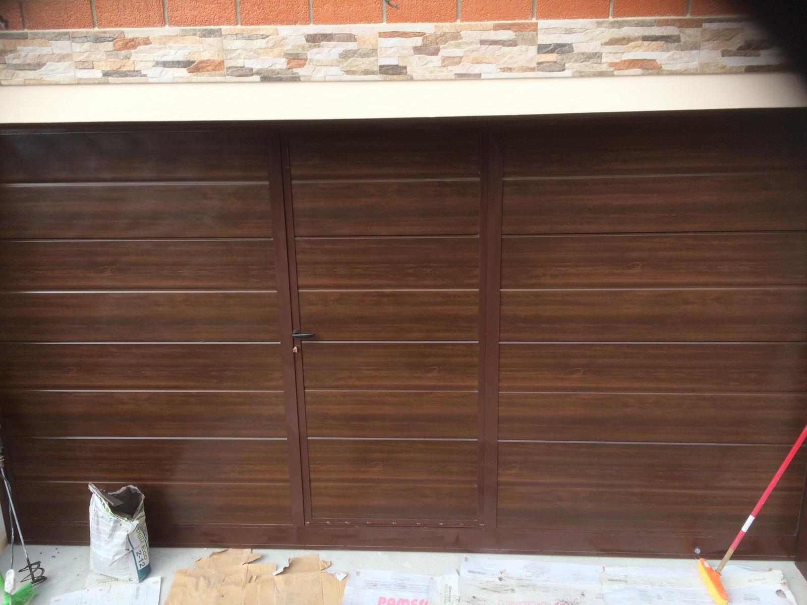 Porta da garage in metallo marrone con linee orizzontali e porta pedonale centrale.