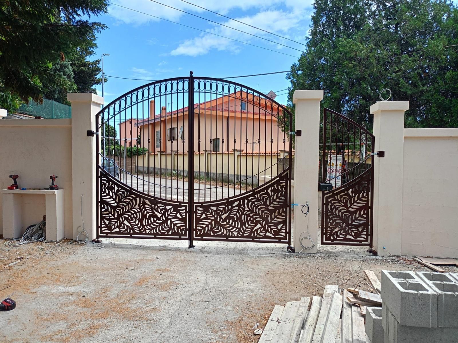 Recinzione in metallo nero e oro con dettagli circolari e pinnacoli, sullo sfondo di un campo verde sfumato e del cielo.