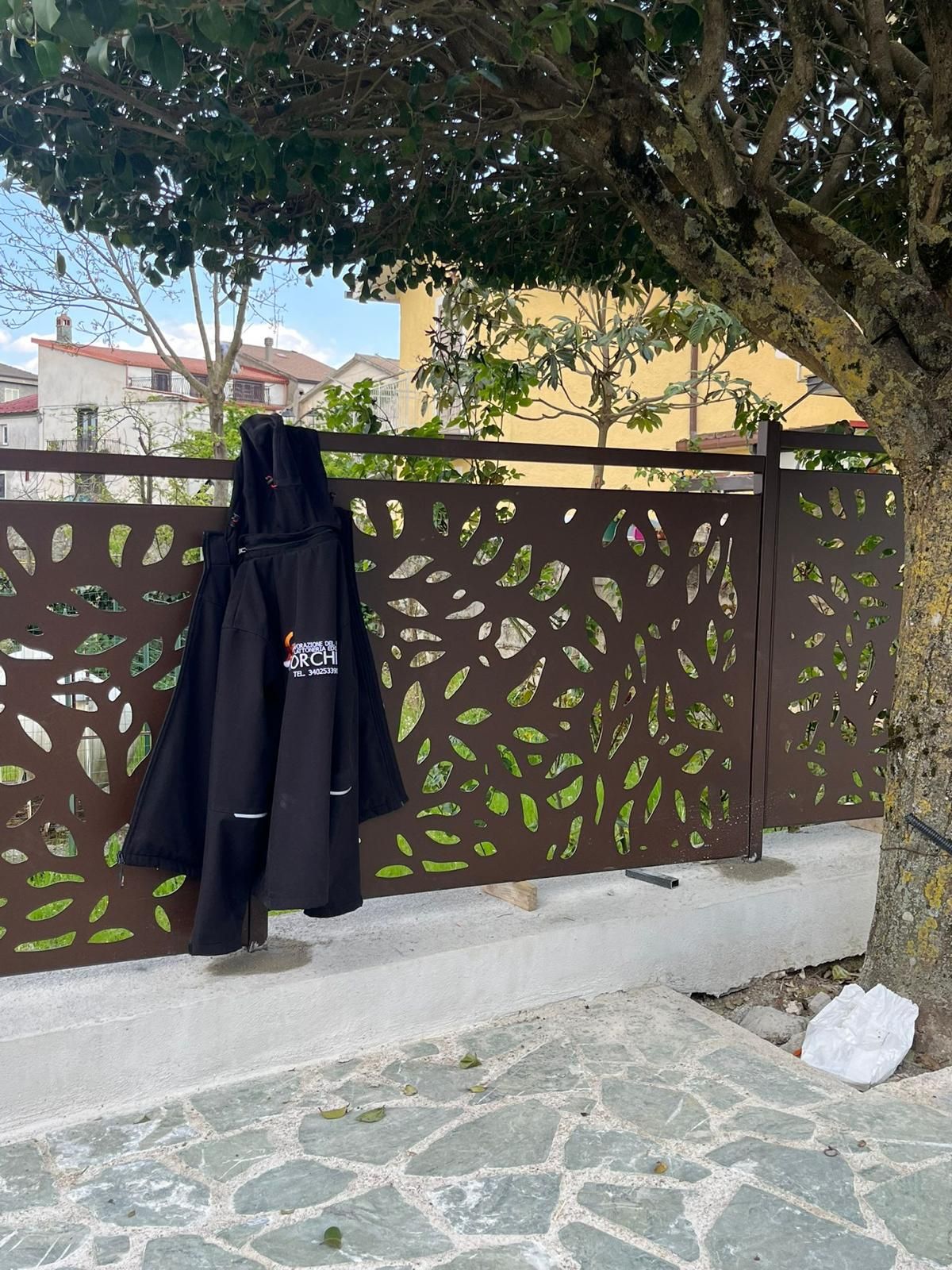 Recinzione decorativa in metallo nero con volute bianche. Muro in pietra e sentiero sullo sfondo.