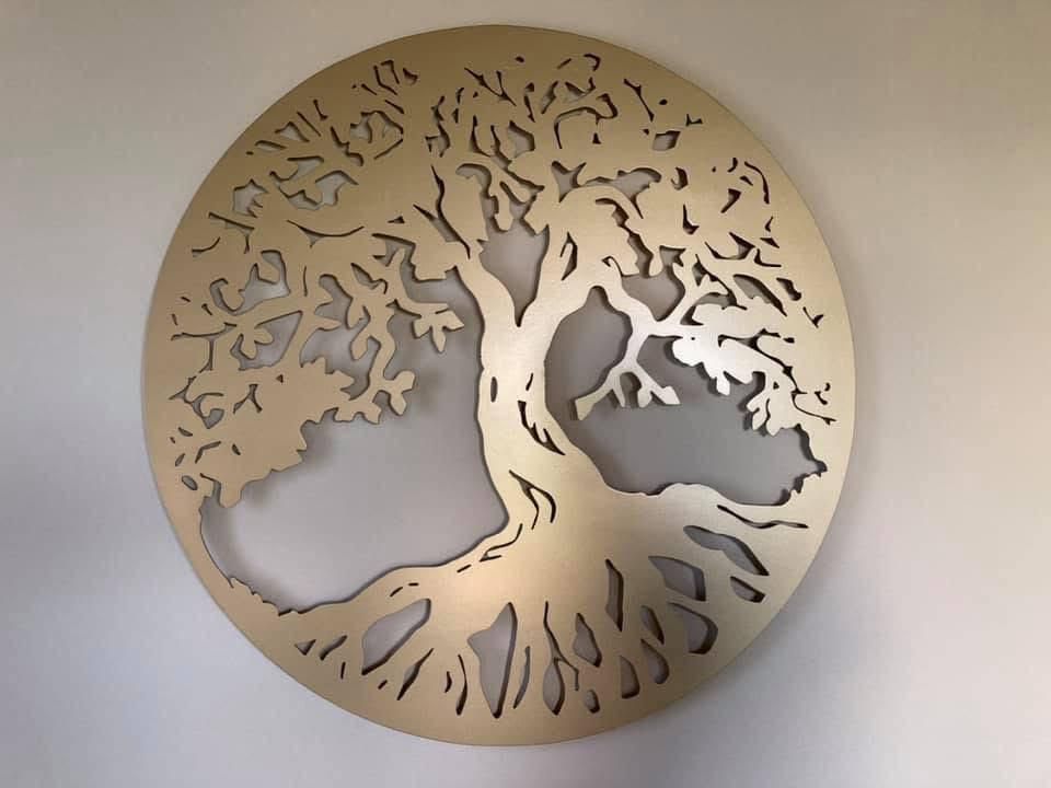 Scultura in metallo raffigurante una vite con foglie e uva, appoggiata su una parete arancione.