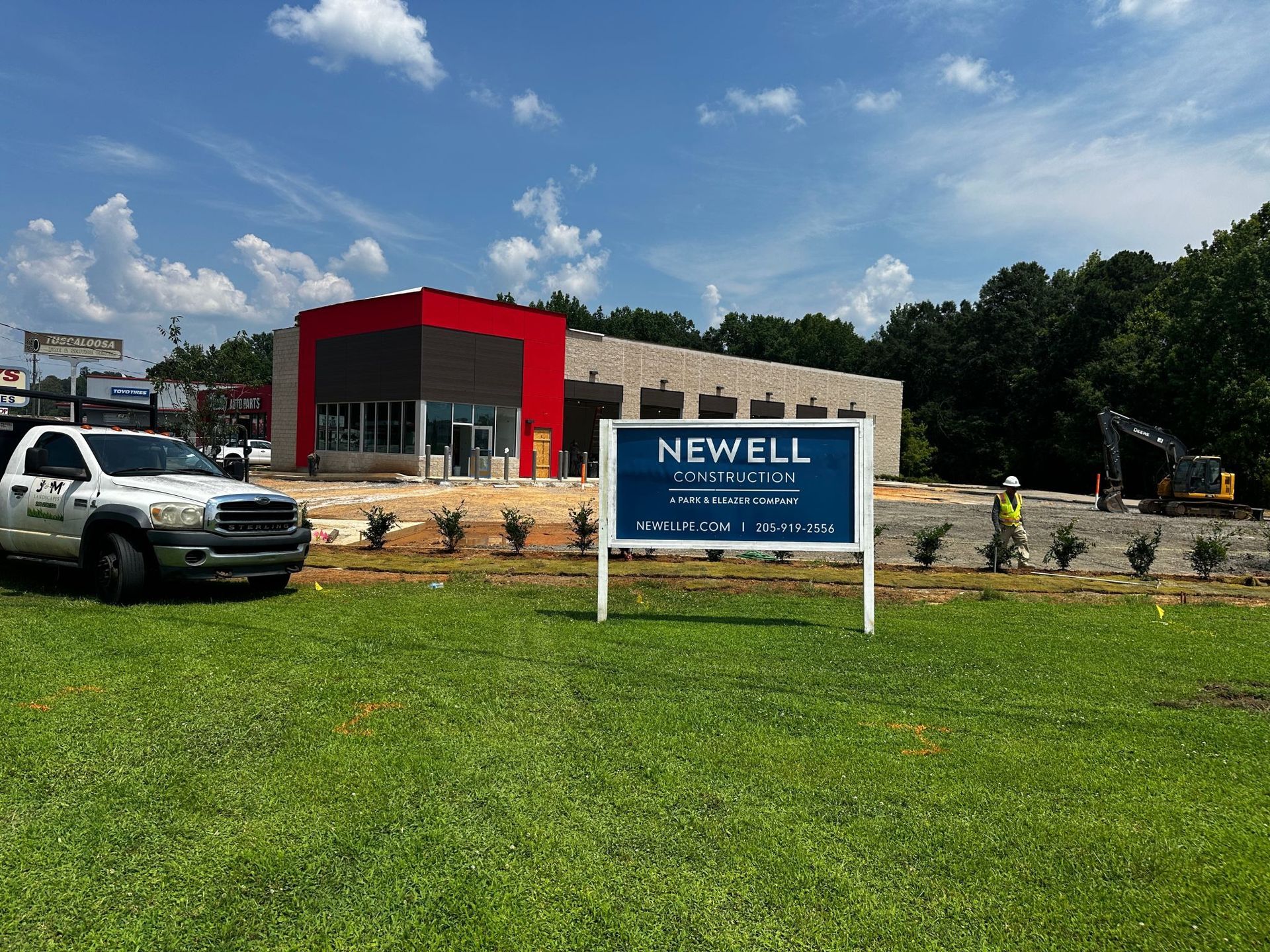 Newell Co. under construction. Building with red and gray accents, a sign, truck, and a worker.