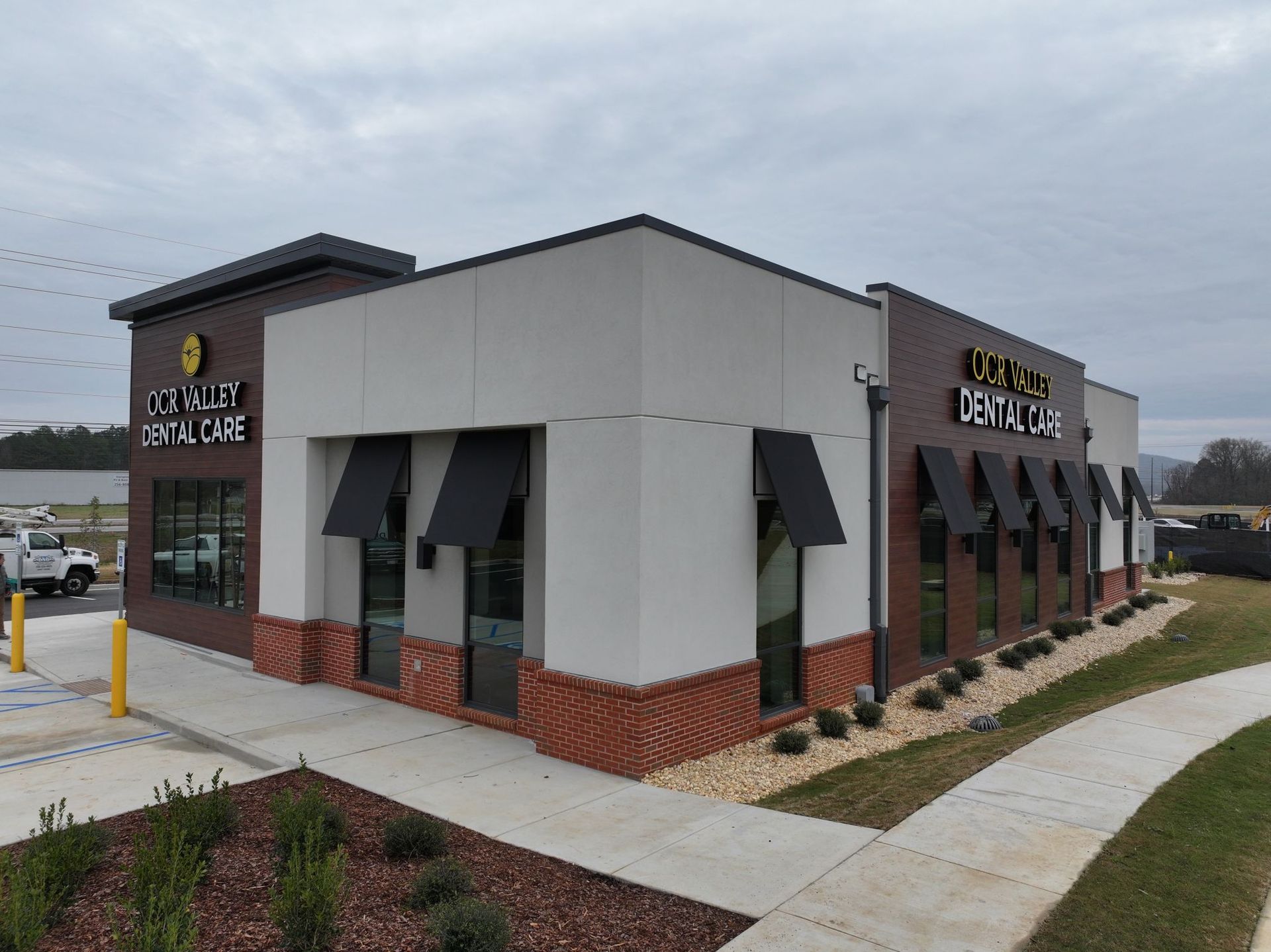Modern dental office with brick facade, large windows, and awnings under cloudy skies.