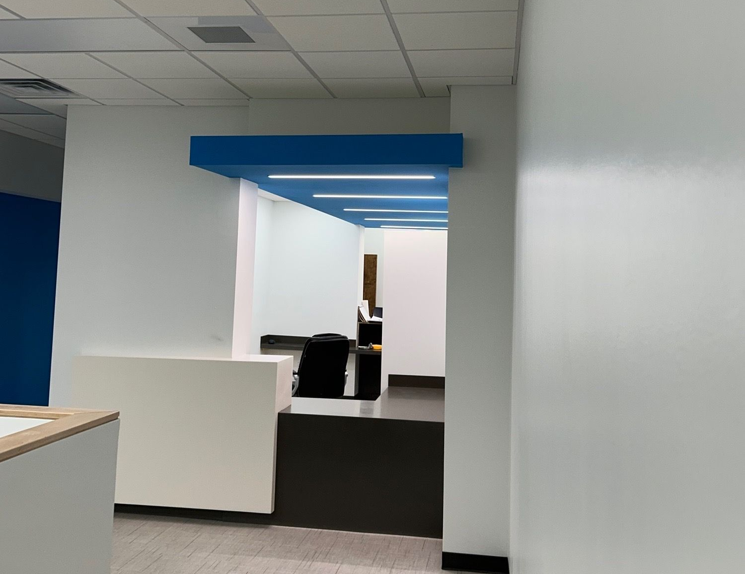 Office interior with blue accents, white walls, and a glimpse into a work area.
