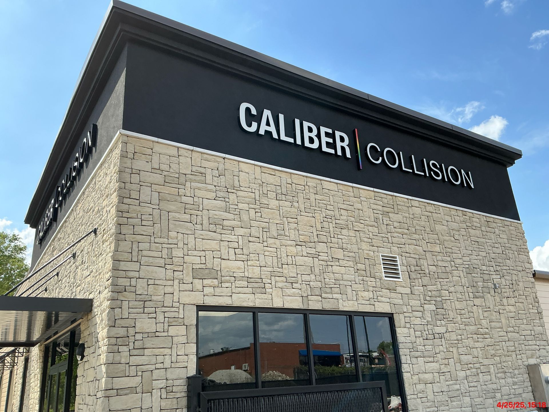 A Caliber Collision auto repair center with a tan stone facade and black trim against a bright blue sky.
