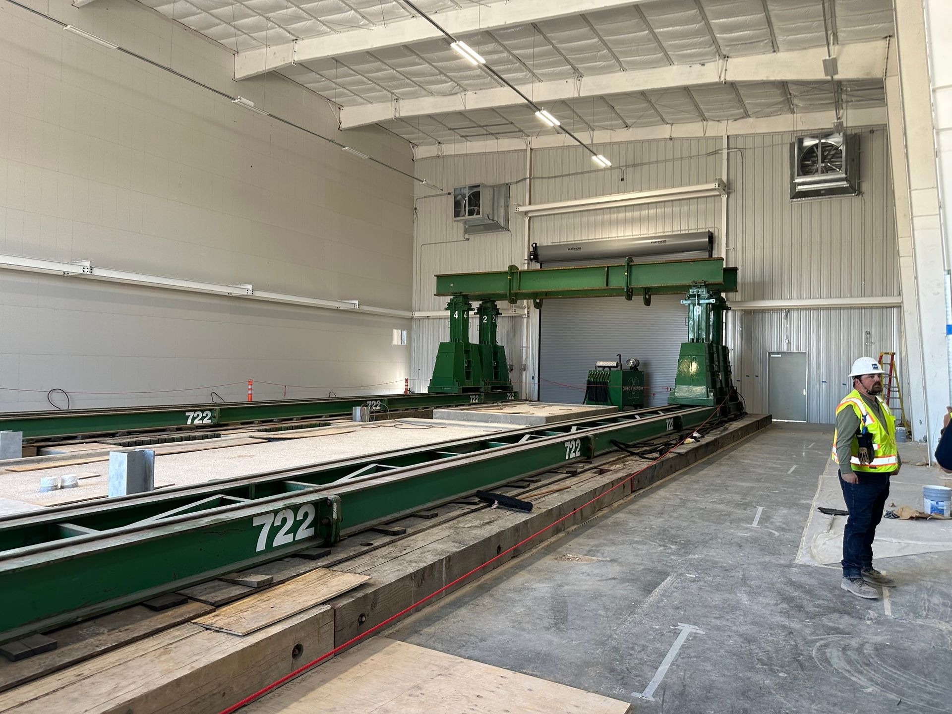 A large green industrial machine inside a warehouse. A man in a vest stands near the machine.