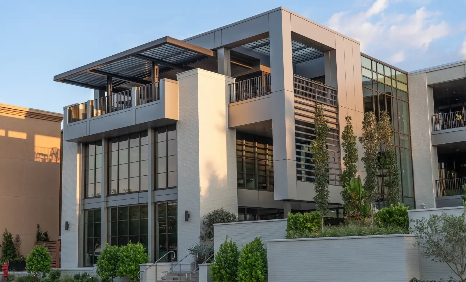 A modern, multi-story commercial building featuring gray concrete, large glass panels, and a rooftop terrace with greenery.
