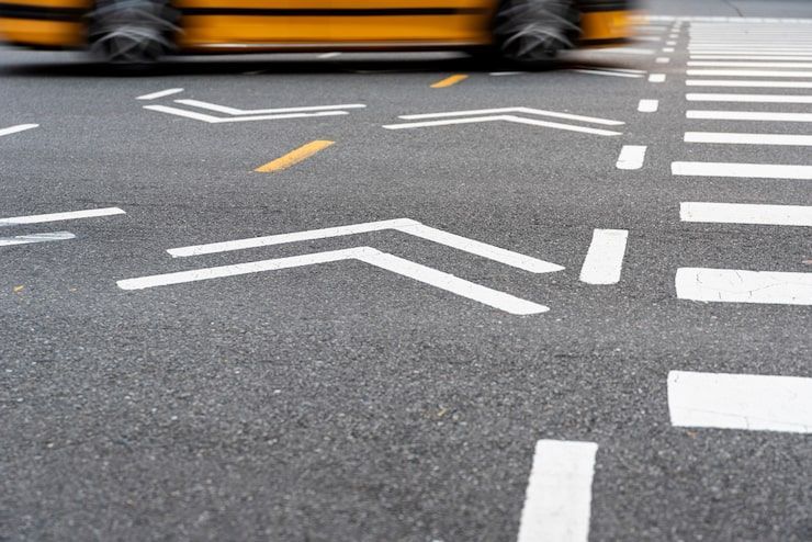 A blurred yellow taxi crosses an intersection marked with white chevron lane guidelines and a crosswalk.