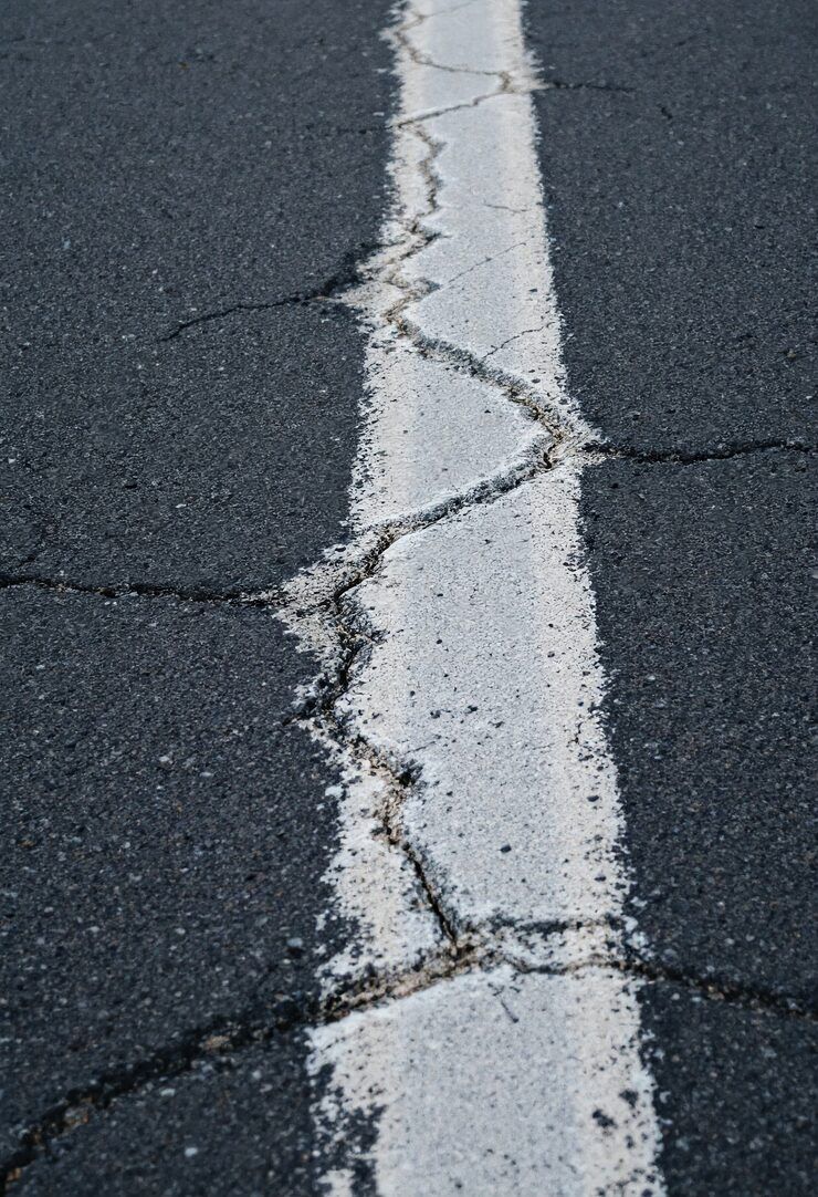 A white painted line on dark asphalt, showing significant weathering and branching cracks along its surface.