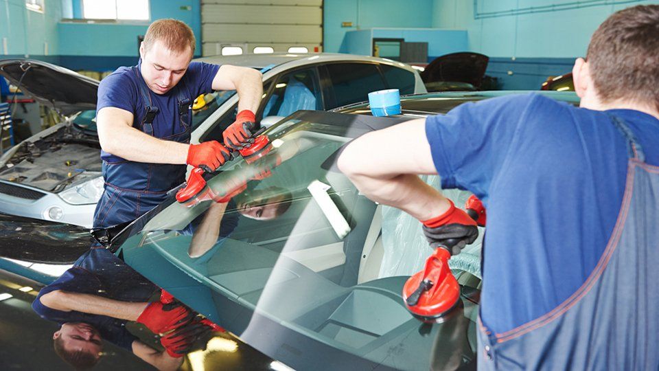 two men are working on a car windshield in a garage