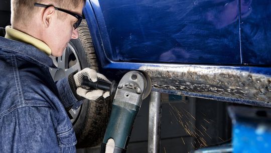 a man is using a grinder on the side of a blue car