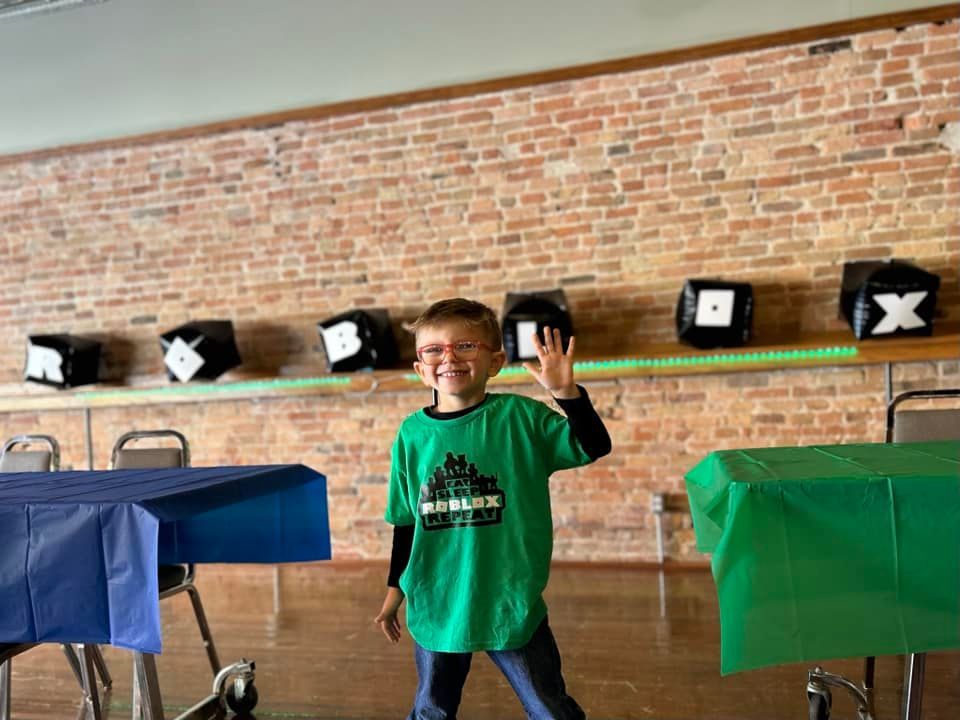 A young boy in a green shirt is standing in front of a brick wall.