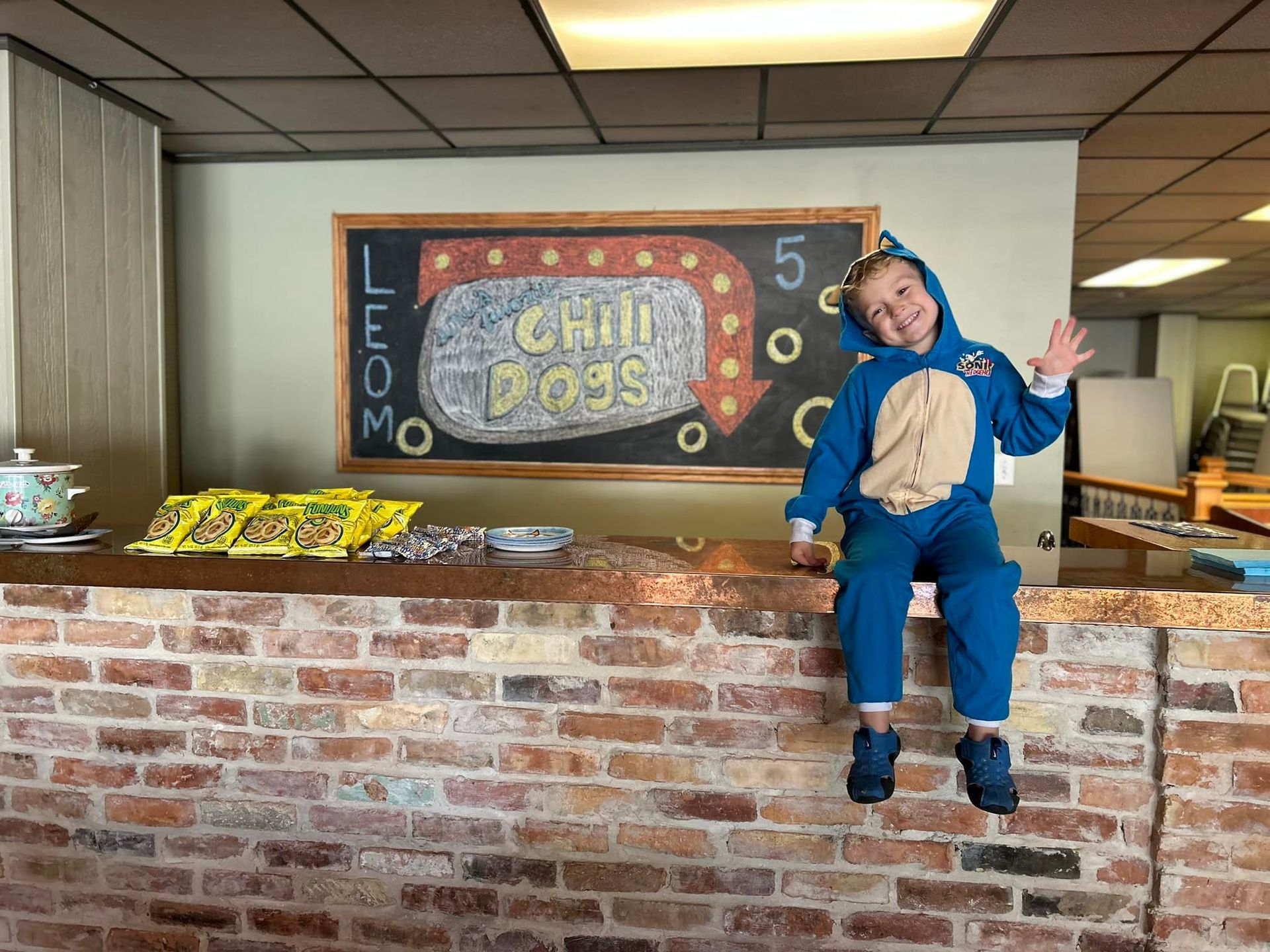 A young boy in a blue onesie is sitting on a counter.