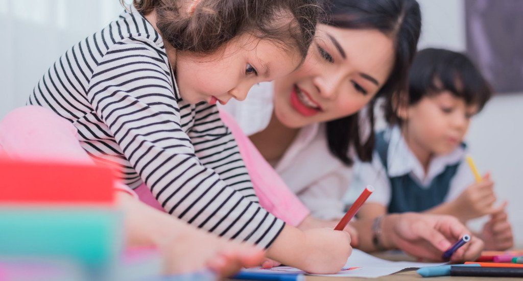 A woman and two children are sitting at a table drawing with markers.