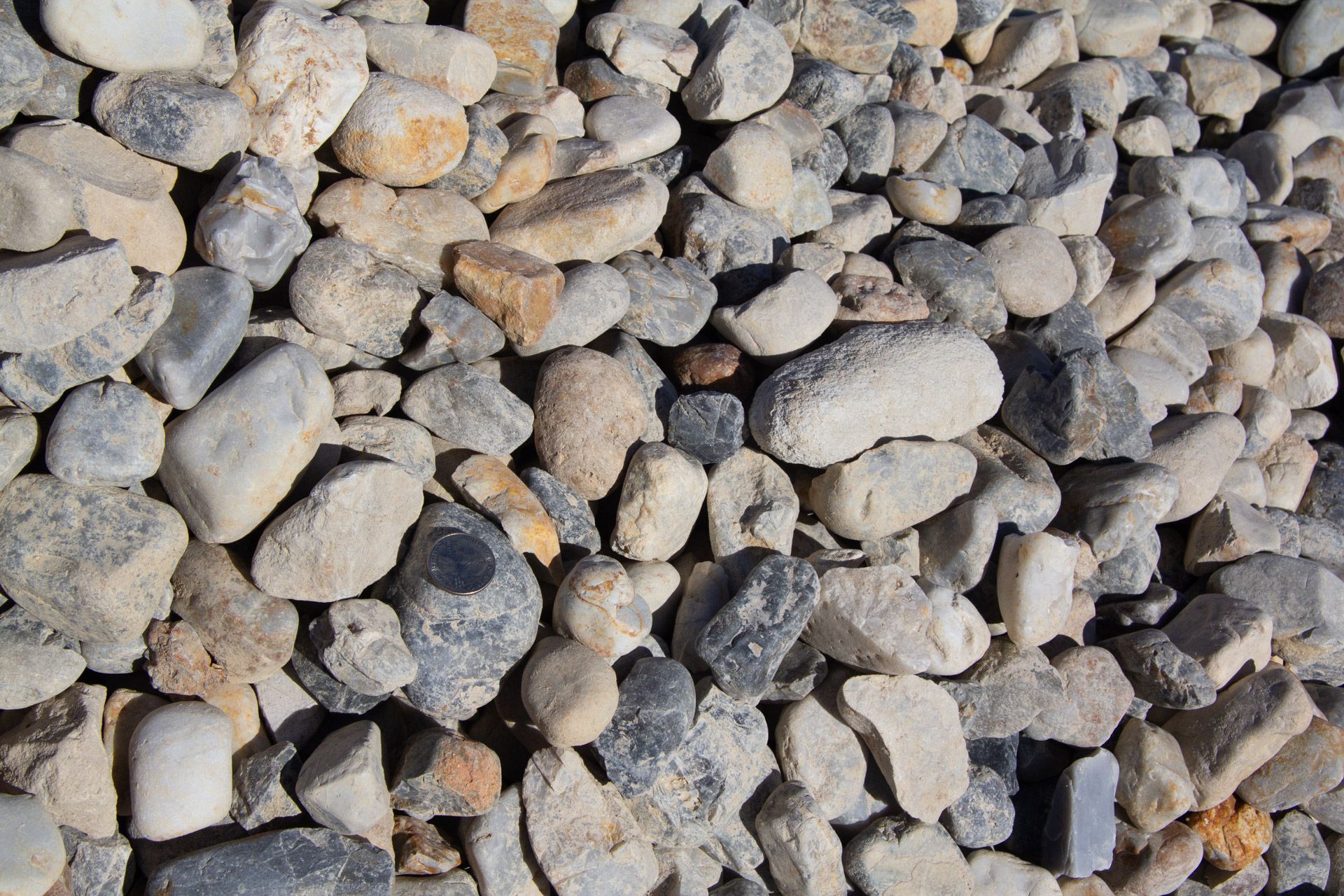 Pile of mixed rounded river rocks, varying shades of gray, tan, and beige.