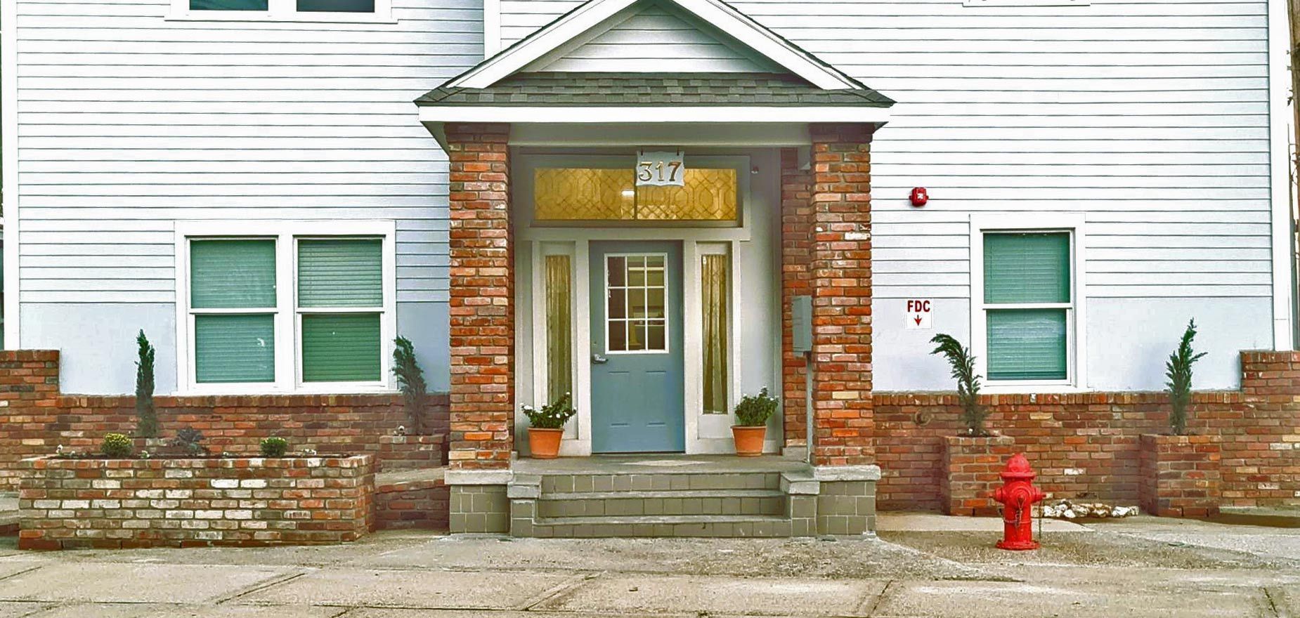 A building with a blue door under a covered porch with a red brick facade, and a red fire hydrant.