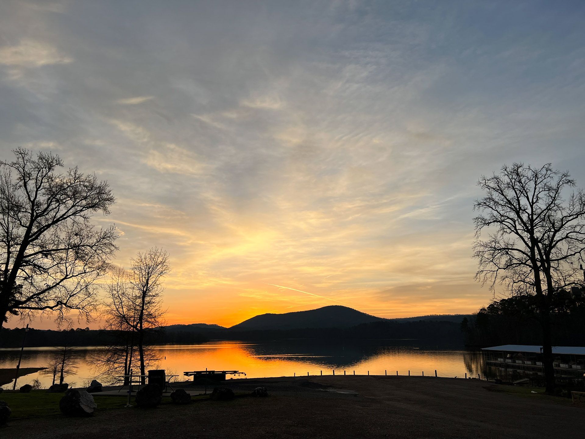Sunset over a lake with mountains in the distance; orange and yellow hues in the sky.
