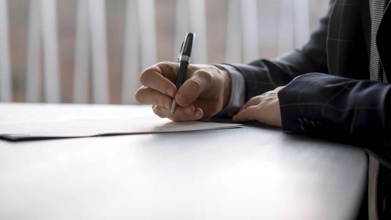 A man in a suit is writing on a piece of paper with a pen.