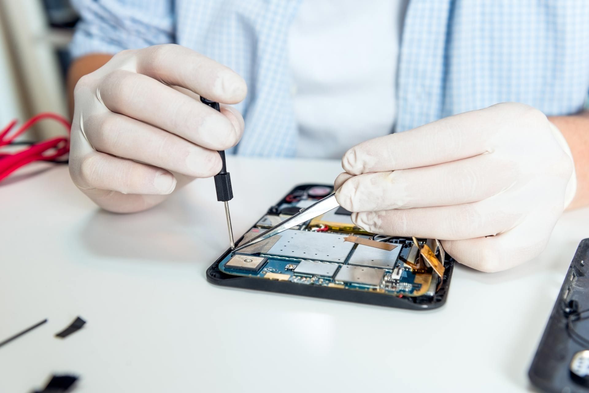 Person repairing a disassembled smartphone using tools, wearing gloves, indoors.